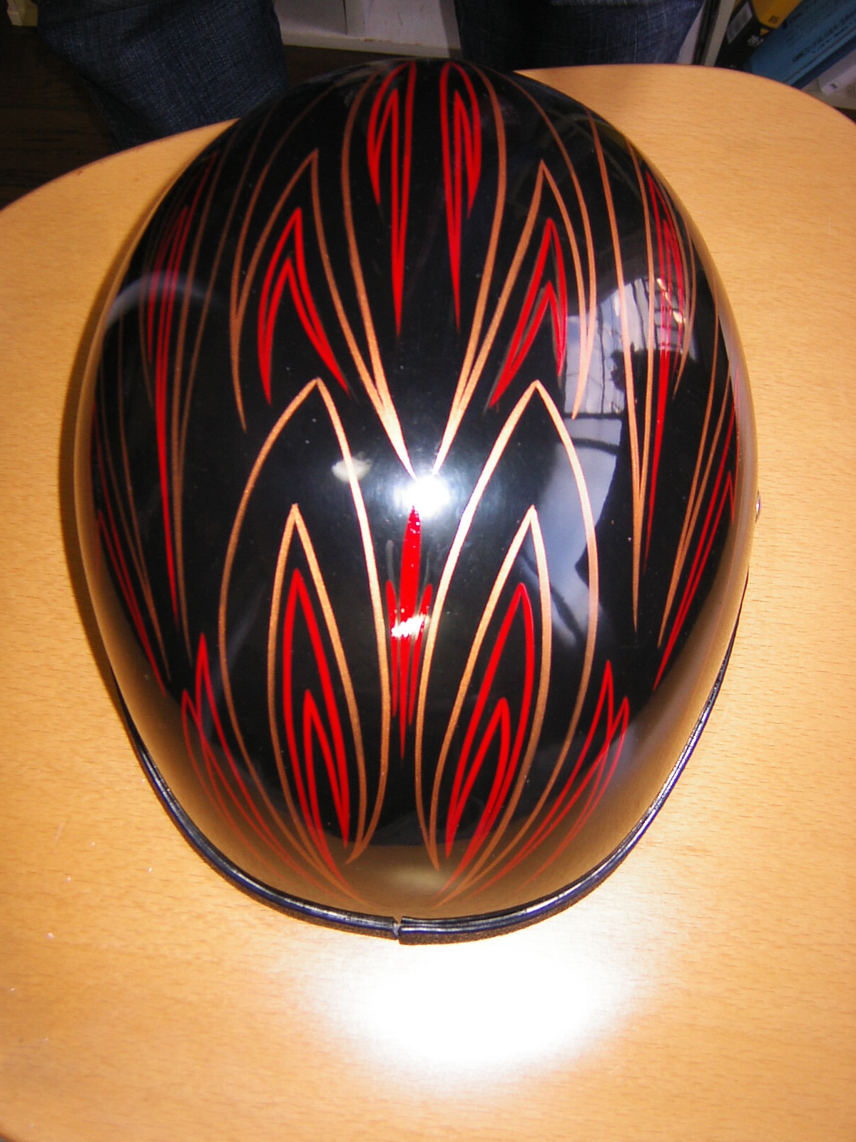 Black motorcycle helmet with red and tan pinstriped flame artwork, photographed on a wooden table