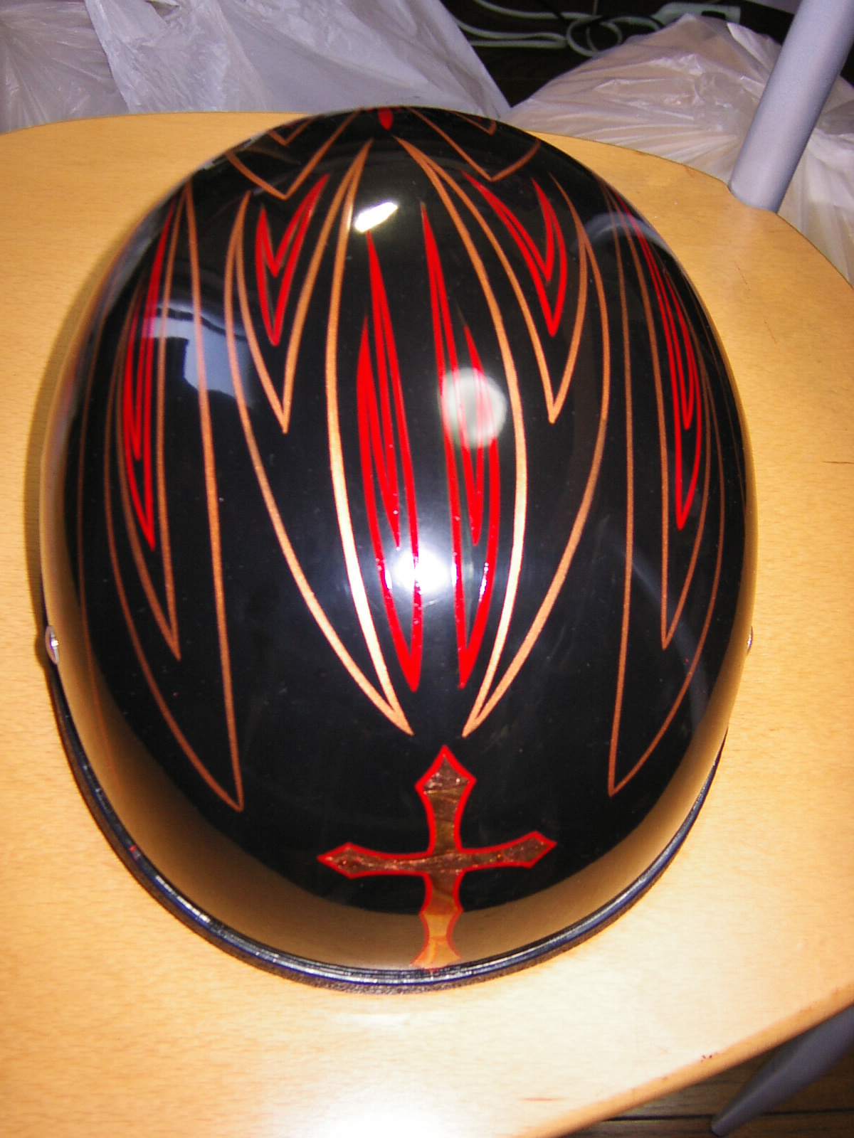 Black motorcycle helmet with red and tan pinstriping and a small cross design, sitting on a wooden table
