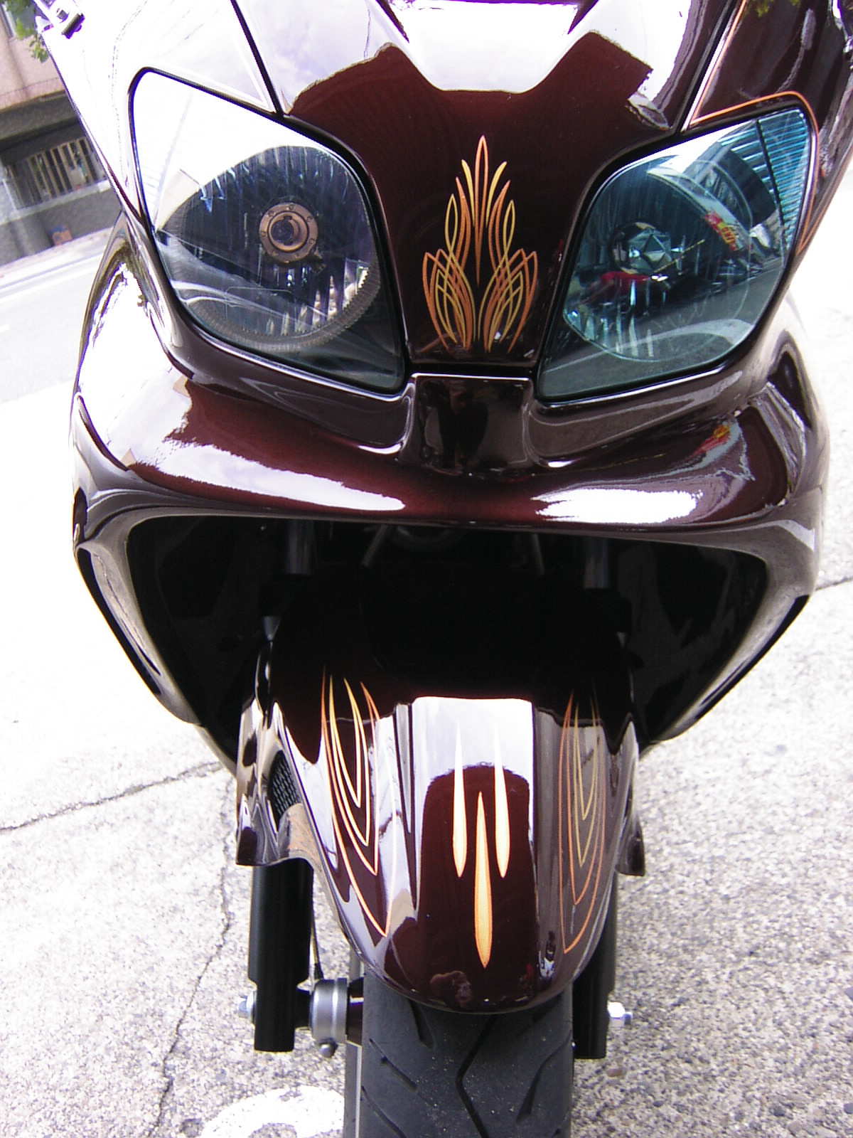 Close-up front view of a dark red motorcycle fairing with gold flame pinstriping and dual headlights