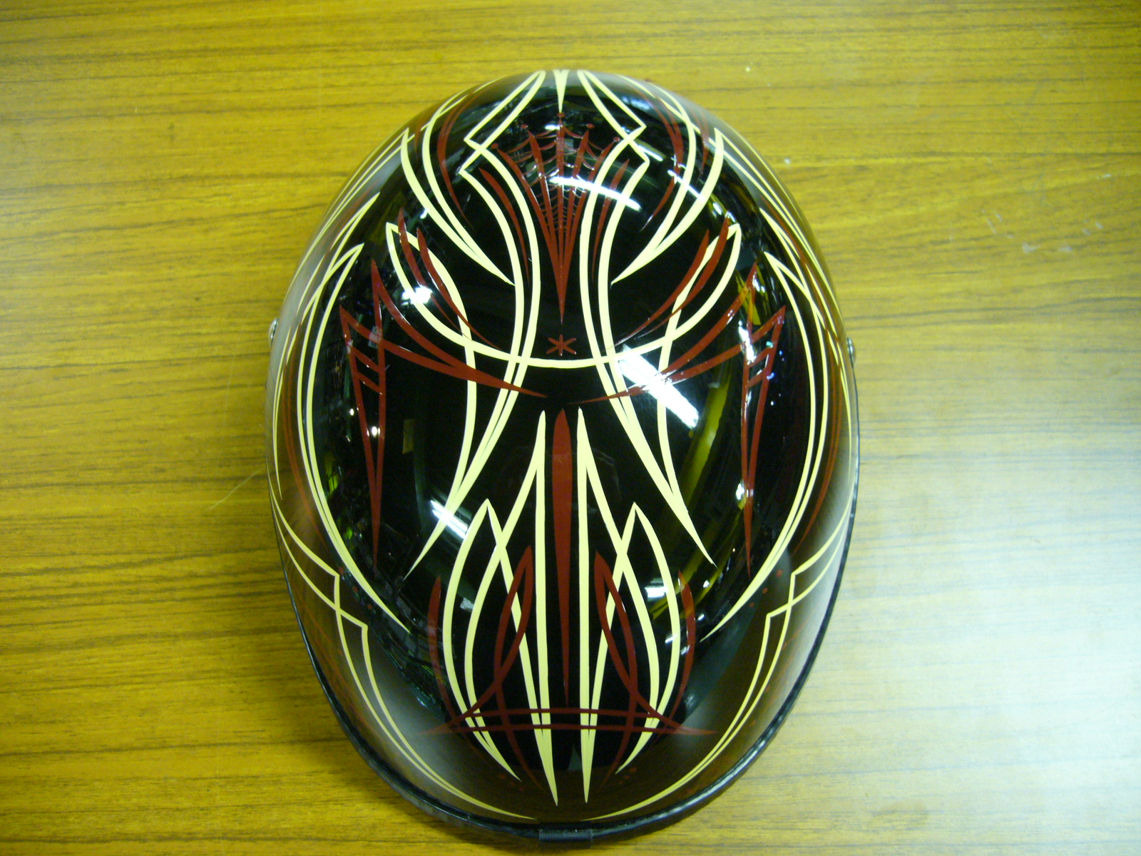 Black full-face motorcycle helmet with intricate cream and dark red pinstripe flame design, photographed from above on a dark surface